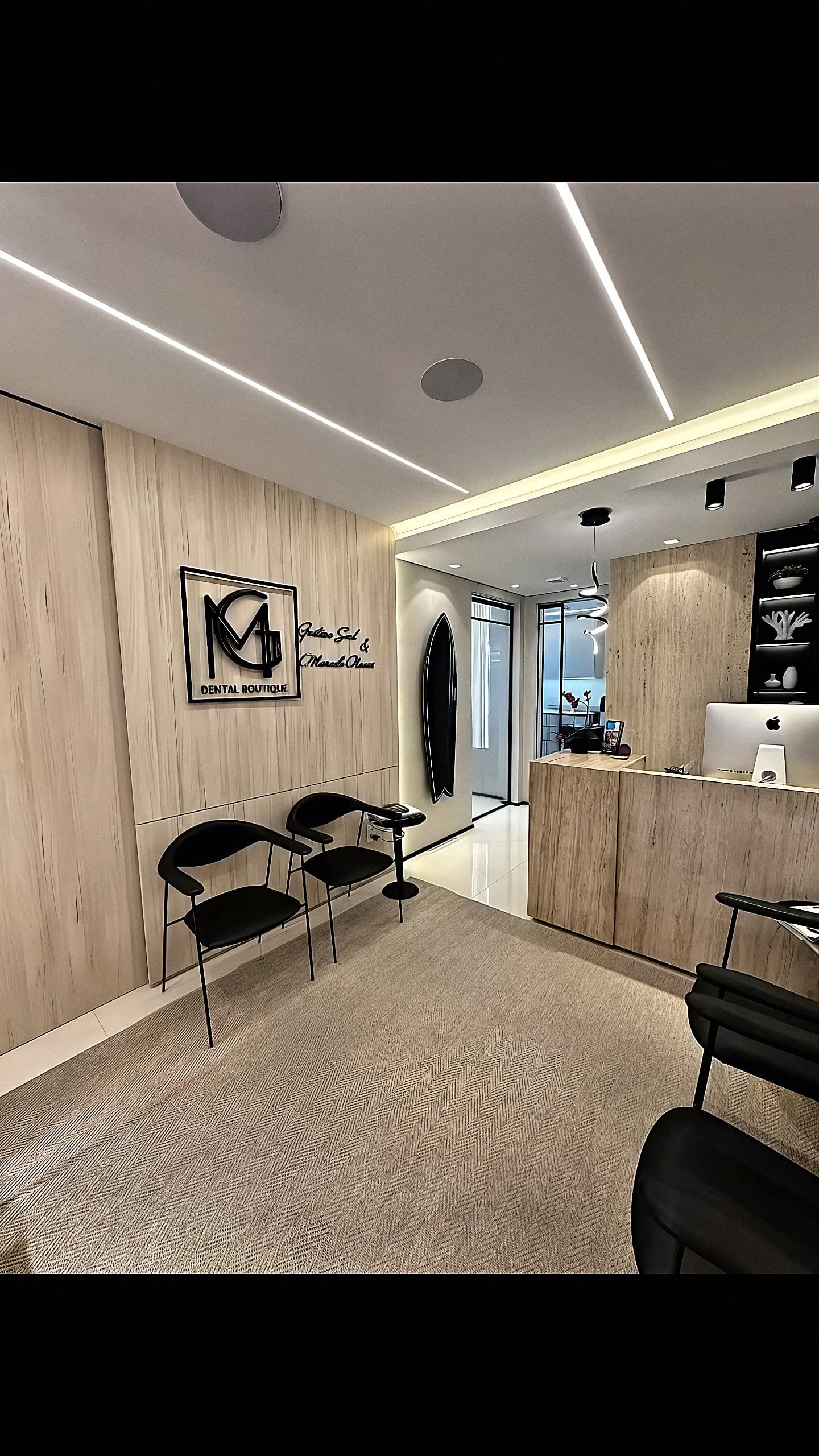 Recepção da GM Dental Boutique com painéis de madeira clara, travertino e prancha de surf na parede